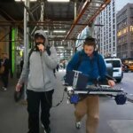 Street performance setup with a musician singing into a microphone and another musician playing a mobile electronic rig on a city sidewalk, ariathome artist style.