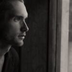 Side profile portrait of a man gazing out a window in black and white.