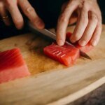 Close-up of hands slicing fresh tuna on a wooden cutting board, perfect for Asian cuisine themes.