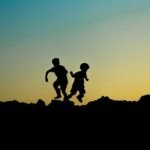 Silhouette of two children joyfully playing outdoors at sunset, capturing a moment of adventure.