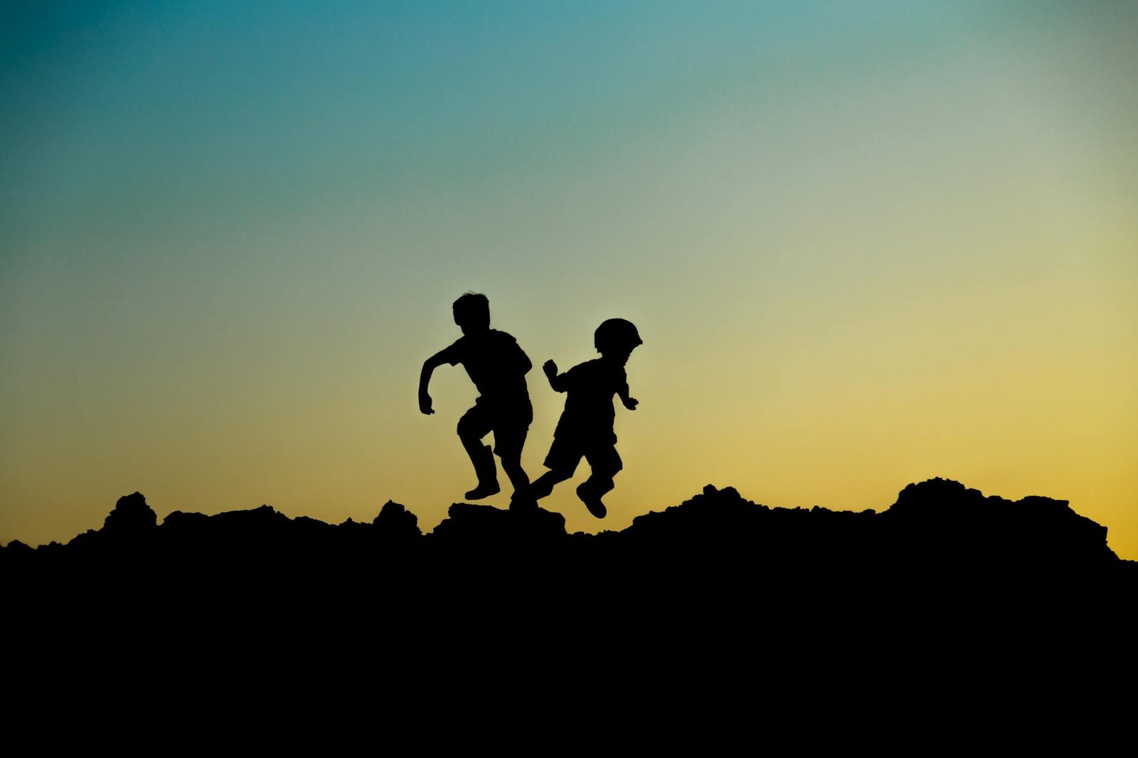 Silhouette of two children joyfully playing outdoors at sunset, capturing a moment of adventure.