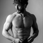 Black and white portrait of a muscular man with curly hair and beard, showcasing strength.