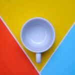 Overhead shot of a white mug on vibrant red, yellow, and blue background. Perfect for design and modern themes.