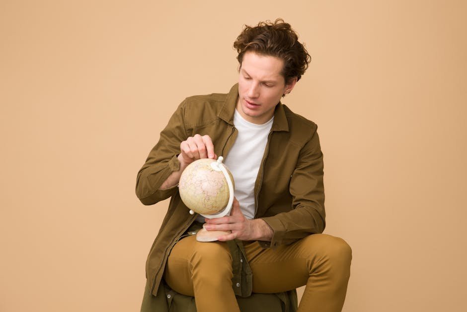 Adult man studying a globe, sitting down, wearing casual attire indoors.