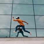 A man in motion jumps against a glass facade, creating a dynamic urban reflection.