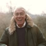 A smiling elderly man enjoying the outdoors in a fur-lined coat, exuding warmth and happiness.