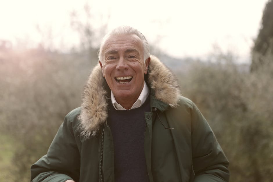 A smiling elderly man enjoying the outdoors in a fur-lined coat, exuding warmth and happiness.