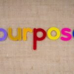Colorful felt letters spelling 'purpose' on a textured fabric background with ample copyspace.