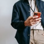 A man in casual attire browsing on a smartphone indoors, showcasing modern tech lifestyle.