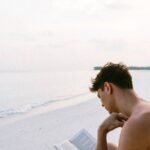 A man enjoys reading a book on a serene Maldives beach, capturing the essence of relaxation.
